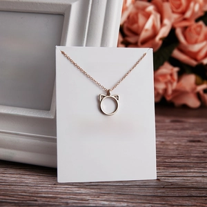 Minimalist cat ear necklace on a gift card with pink roses on a dark wood background