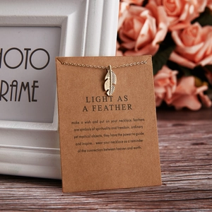 Detailed view of a gold feather pendant necklace on a poetic gift card display