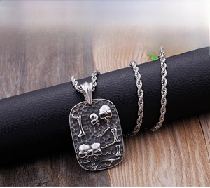 Macro shot of punk style rectangular skull pendant with embossed bone details on twisted chain