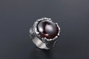 Detail of silver dragon claw ring holding a round red gemstone with polished finish