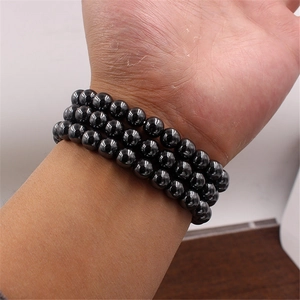 Detailed view of triple-layered black magnetic stone bracelet with crown charm on wrist