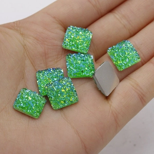 Close-up of 12mm green resin square charms with glitter texture held in hand