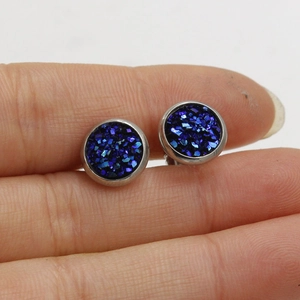 Deep blue 8mm stainless steel stud earring with shimmering finish held by fingers