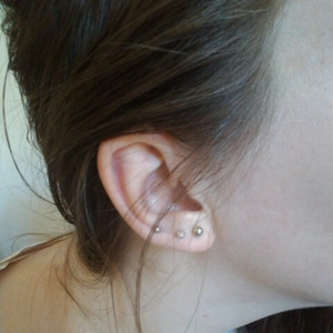 Detailed view of three small golden ball earrings made of 316L stainless steel on ear