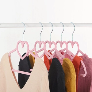 Pink heart-shaped non-slip plastic hangers holding colorful sweaters on white wall