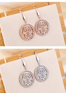 Detail view of Hamsa Hand crystal earrings in rose gold and silver finishes on a stand