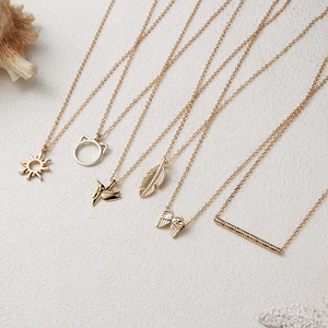 Set of six gold-tone alloy necklaces with sun, cat, and feather pendants on beige surface