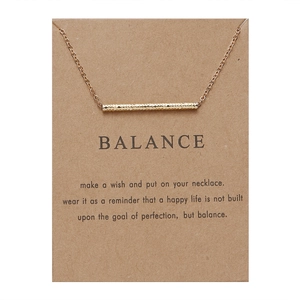 Close-up of gold bar pendant necklace on Balance wish card with inspirational text