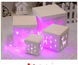 Detail of four white cutout Christmas gift boxes with reindeer patterns and LED lights