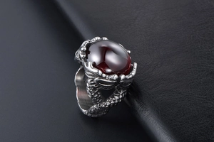 Close-up of double dragon ring with a large polished dark red gemstone on black leather