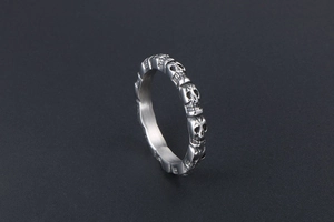 Macro detail of silver stainless steel ring featuring embossed skull patterns on black background