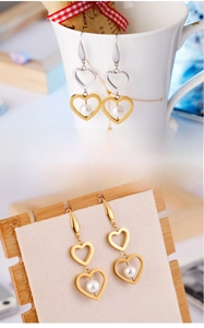 Détail des boucles d'oreilles en acier titane en forme de cœur avec perles blanches