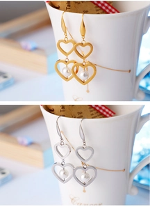Détail de boucles d'oreilles cœur en acier titane avec perles blanches en or et argent