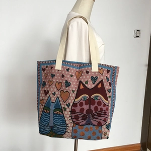 Detail of pink woven tote bag with blue cat patterns and heart motifs on shoulder strap