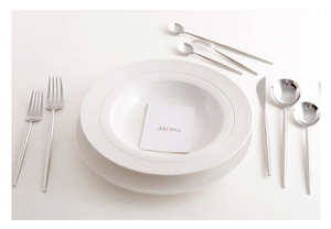 Close-up of white ribbed ceramic dinnerware set with elegant silver cutlery and accessories