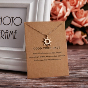 Golden sun pendant necklace on kraft paper card with Good Vibes Only message on wood table