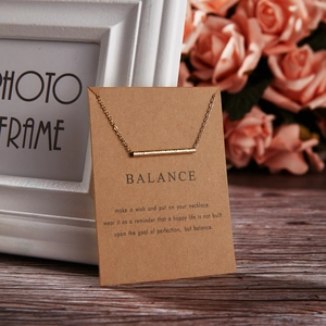 Detail of gold bar necklace on Balance card with floral background and wooden desk