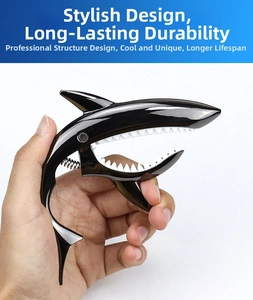 Handheld view of black shark-shaped guitar capo with metal spring and white silicone teeth