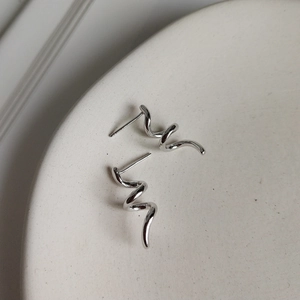 Close-up of minimalist 925 sterling silver spiral stud earrings on white ceramic