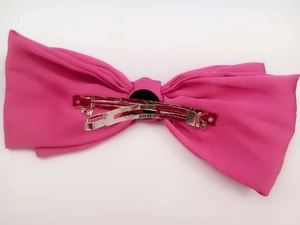 Detail of pink satin bow hair clip featuring a silver metal spring clasp with engraving