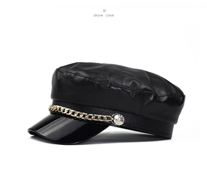 Detail of black PU leather baker boy hat with glossy visor and gold chain strap accent