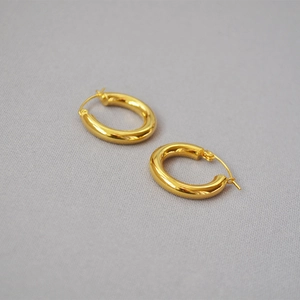 Detailed close-up of golden thick oval hoop earrings with a polished metallic finish