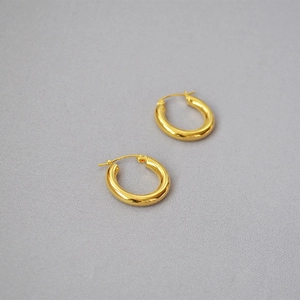 Detail of polished gold brass hoop earrings on a light gray fine textured fabric background