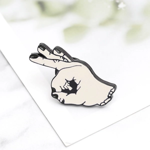 Detailed view of an OK gesture enamel pin with minimalist black and white finish