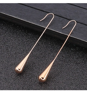 Detailed macro view of elegant rose gold teardrop earrings on dark wood texture background