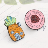 Detail of enamel pins featuring a pineapple house and pink treat people with kindness design