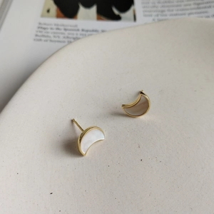 Detailed view of moon-shaped silver earrings with shell inlay on a ceramic plate
