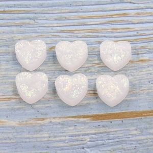 Macro shot of white heart-shaped resin beads with holographic glitter on wood surface