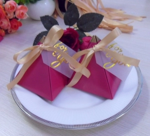 Close-up of magenta pyramid-shaped wedding candy boxes with gold ribbons and labels