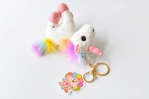 Close-up of white plush unicorn keychain with rainbow mane and golden metal clip