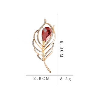 Detailed view of a gold-toned feather brooch with red crystals, measuring 6.3cm by 2.6cm
