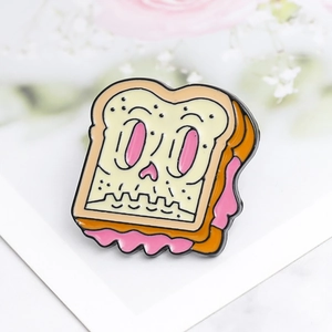 Macro detail of enamel bread slice pin with skull face on minimalist card background