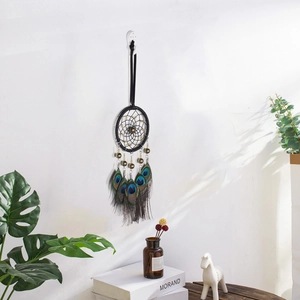 Handmade black dream catcher with peacock feathers and beads hanging on a white wall