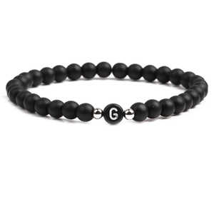 Detail of matte black beaded bracelet with letter G charm and silver metal spacers