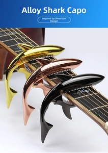 Three shark-shaped metal guitar capos in gold, rose gold, and black on a guitar neck