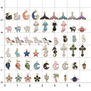Assorted gold enamel charms with moon star and leaf shapes on a white ruler background