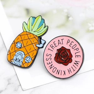 Detail of pineapple house enamel pin and pink badge with Treat People With Kindness text