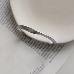 Dettaglio del bracciale ritorto argento opaco su un libro e un piatto in ceramica