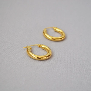 Close-up of polished thick gold plated brass hoop earrings on a light grey fabric background