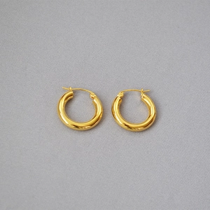 Close-up of a pair of chunky gold brass hoop earrings on dark textured fabric
