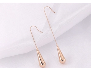 Macro detail of rose gold waterdrop earrings on soft white textured fabric background