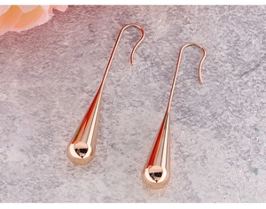 Close-up of rose gold teardrop earrings on a silver textured surface with pink floral decor