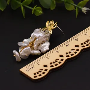 Orecchini a perla barocca naturale con design floreale dorato su sfondo nero intenso