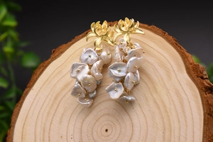 Dettaglio di orecchini con perle barocche pendenti e perni dorati su base in legno