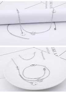 Detail of layered silver anklet set featuring clover, infinity and heart charms