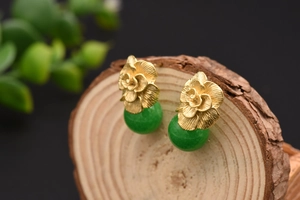 Detailed view of vintage gold flower earrings with green jade beads on a wood stand